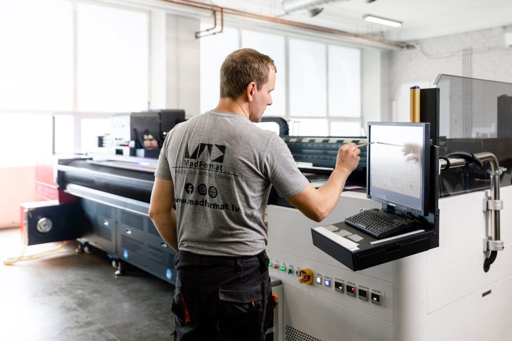 Оператор MADFORMAT у широкоформатного УФ-принтера в цехе в Риге